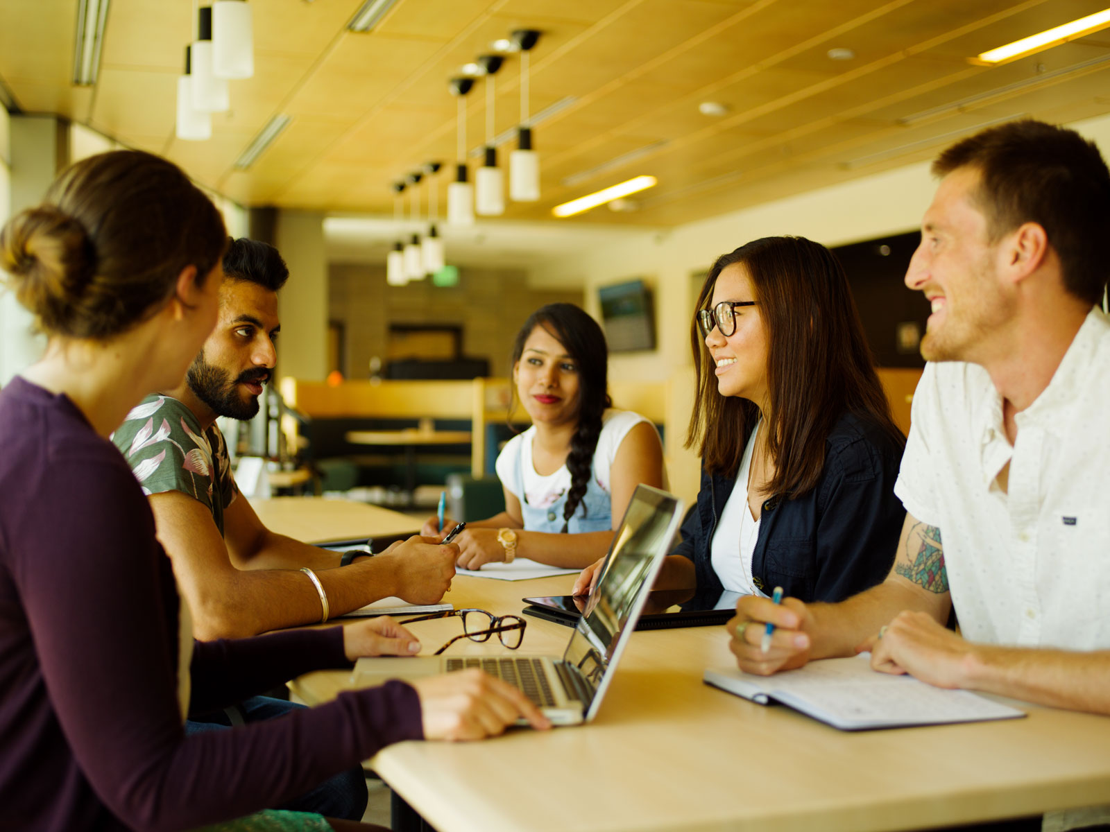 five students sitting at a table talking and studying