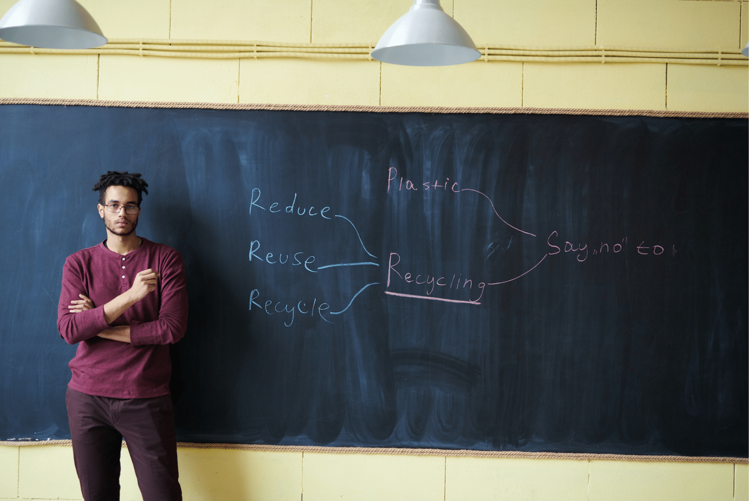 A man facing the camera stands in front of a chalkboard that contains a handwritten cloud diagram with the words 