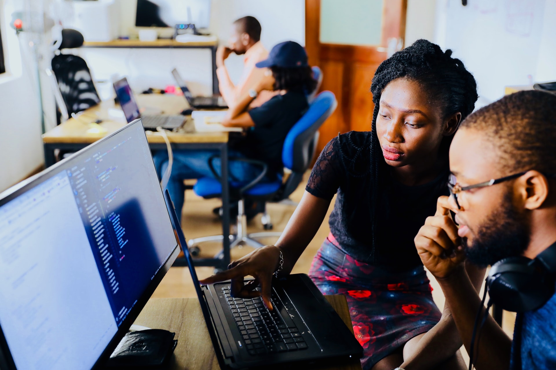 A man working on computer code while a woman stands next to him to help.