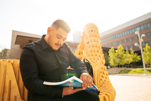 A male student reading his textbook outside