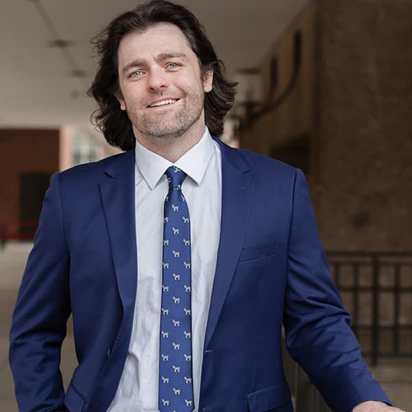 Jordan Arellanes with longer, dark hair, wearing a bright blue suite and tie, smiling with his teeth.