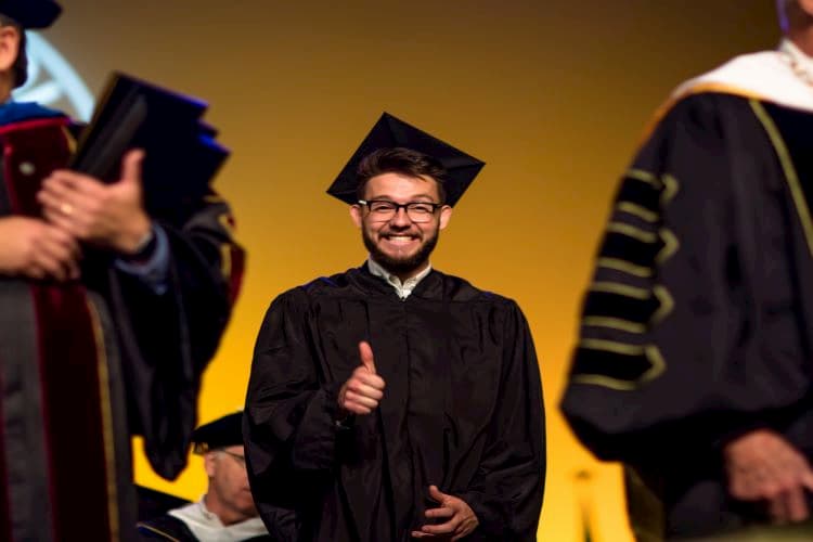 Male graduate smiling and giving a thumbs-up to the camera