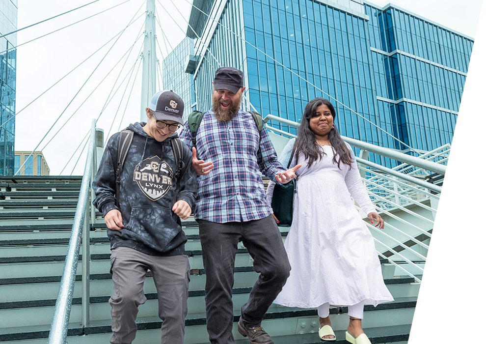 Three students walking down stairs outside discussing a project