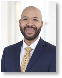 Smiling African-American man with beard and dressed in blue jacket with with shirt and yellow tie.