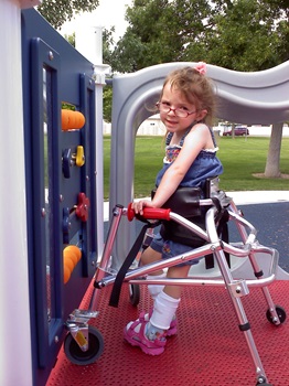 a young girl plays in a playground using her walker