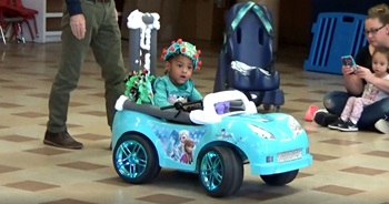 a young girl wears an e e g cap while driving an adapted toy car