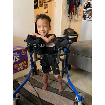 Young child smiling and standing independently using his Gait Trainer.