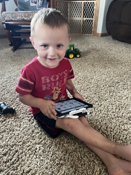Young boy smiling while using his AT device, with Proloquo2Go app, to communicate with others. 