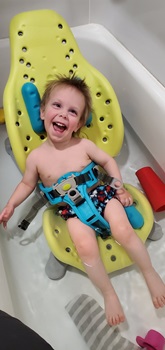 young boy sitting in bathtub, smiling, using the Splashy Chair