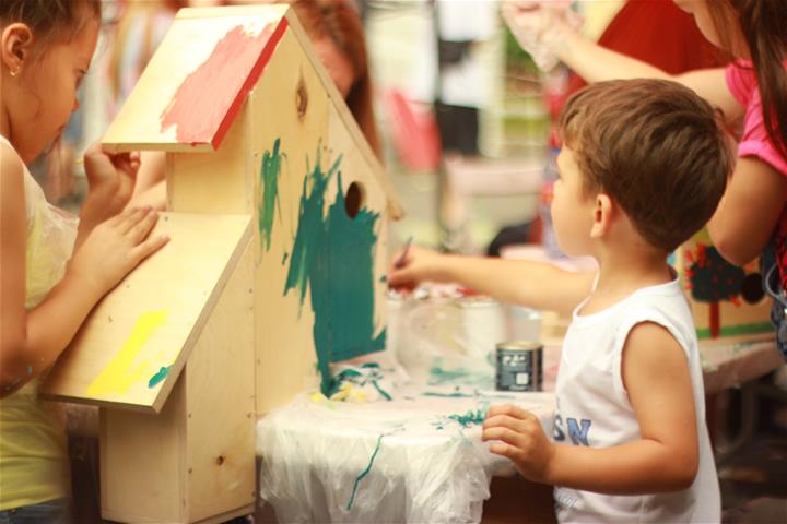 Young children paint a wooden bird house