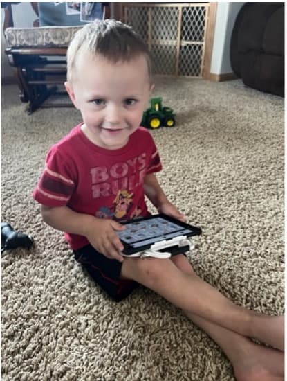 A boy sits on the floor with his iPad communication device